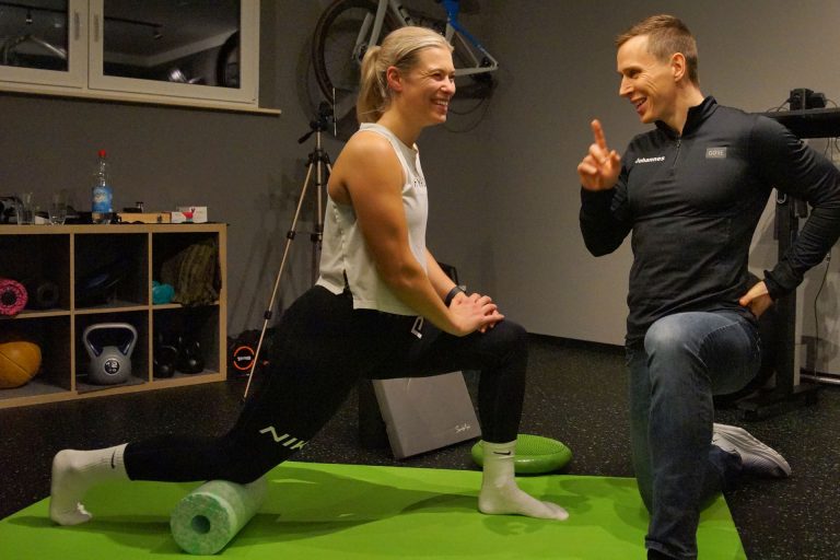 Trainer begleitet eine Sportlerin bei einer Übung auf einer grünen Matte